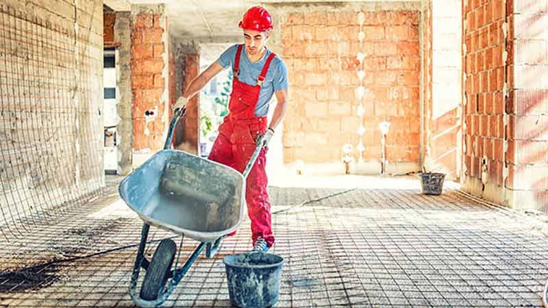 A worker pushing a wheelbarrow on a construction area.