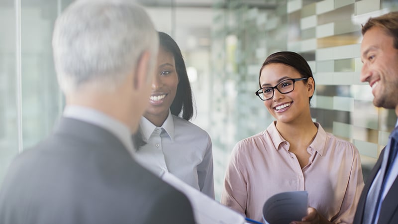 Man speaking to three professionally dressed smiling colleagues.