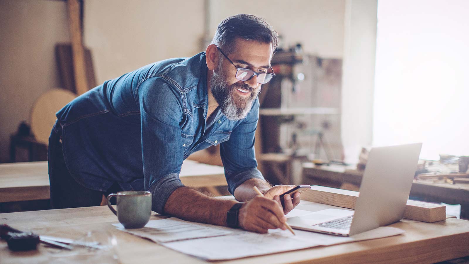 Smiling, casual man with beard, working with pencil, paper and laptop